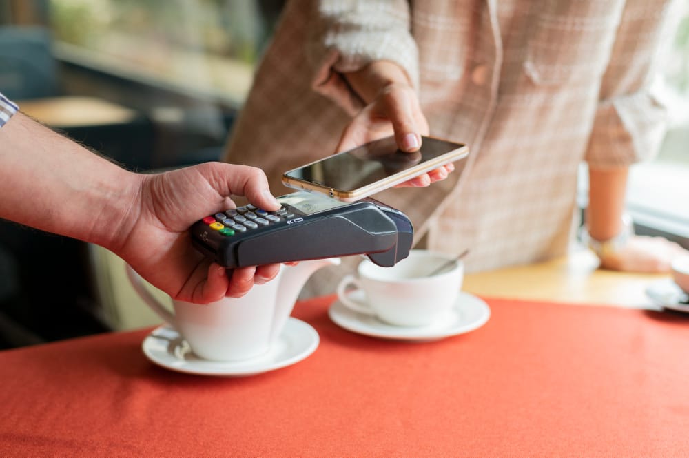 Person making a contactless payment with a smartphone at a café, illustrating the importance of PCI compliance test in securing payment card transactions.