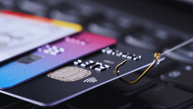 Image depicting credit card fraud with multiple credit cards on a keyboard and a fishing hook symbolizing phishing attacks.