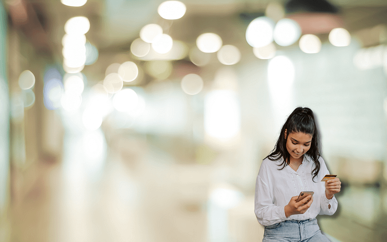 A person in a white blouse and jeans, holding a smartphone and credit card, stands in a softly lit, bokeh-filled space. The scene captures the ease of modern transactions, hinting at an intelligent payment routing guide for seamless, optimized payments.